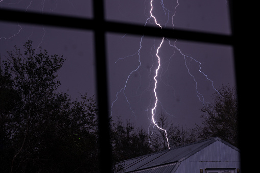 A lighting strike in the distance nearby through inside a home window.