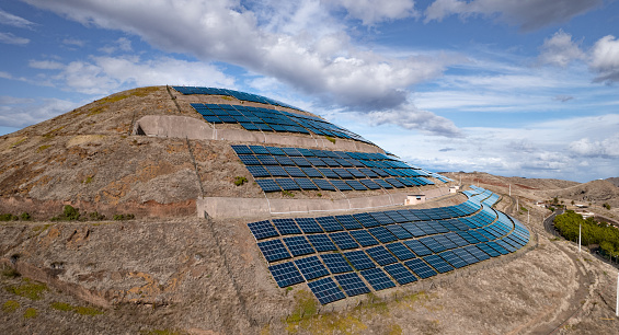 Aerial view of modern solar batteries placed on slope of hill under blue cloudy sky