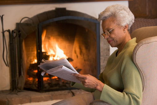 Woman in living room reading newspaper in front of fire