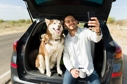 Cheerful young man taking a selfie with his beautiful husky dog while making a road trip together