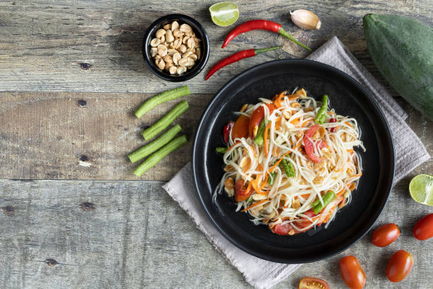 Green papaya salad in a black plate on a wooden table, top view. Top view of Thai food. Green papaya salad in a black plate on a wooden table, top view. Top view of Thai food. tam o'shanter stock pictures, royalty-free photos & images