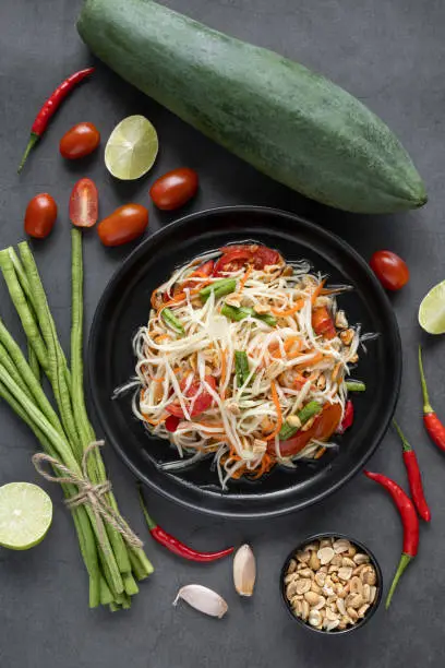Traditional Thai papaya salad and ingredients for its preparation on a gray table, top view.
