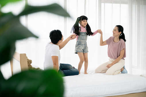 Happy asian family people leisure in bedroom together. Father and mother with daughter relaxing on bed and enjoy funny