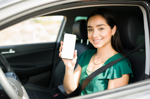 Attractive female driver showing her smartphone screen and ready to pick up a passenger on a ride share app