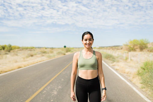 Gorgeous hispanic woman in activewear smiling and looking at the camera while working out outdoors
