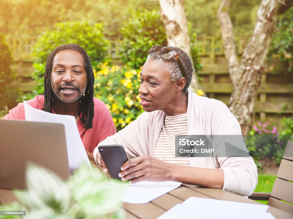 A senior couple using a laptop and going over paperwork in the garden at home. Mature man and woman discussing finance while browsing online with a computer Mobile App Stock Photo