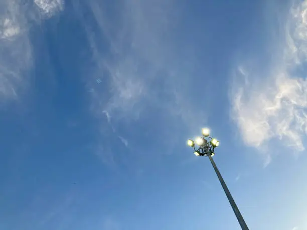 turn-on spotlight post under the clear blue sky and white clouds at a sports complex in the evening