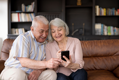 Happy Latin American senior couple watching funny videos at home on a cell phone and smiling â lifestyle concepts