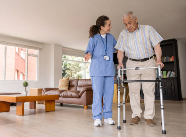istock Home caregiver helping a senior man walk with a walker 1395651964