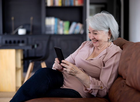 Happy Latin American senior woman watching funny videos at home on a cell phone and smiling â lifestyle concepts
