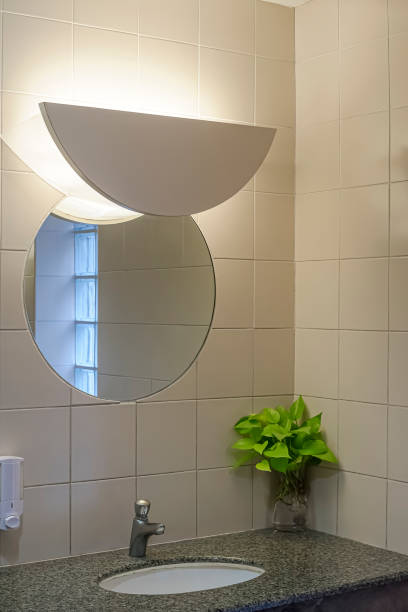 istock Modern wall lamp and circle mirror on beige tile wall with marble counter in luxury restroom 1395655263