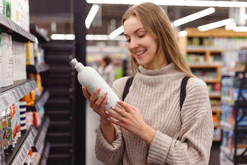 Positive young blonde selecting bottle of shampoo in cosmetics department store