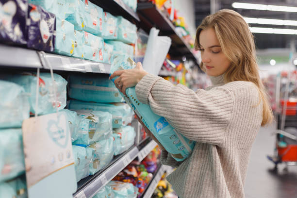 若い女性の母親は、ショップモールのスーパーマーケットでおむつを選びます。子供のための衛生用品 - diaper shopping human pregnancy supermarket ストックフォトと画像