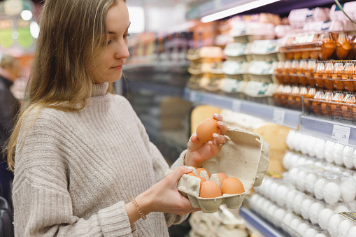Woman chooses chicken eggs in a farm food store. Food consumption, Easter.