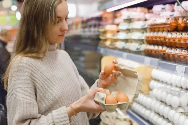 Photo of Woman chooses chicken eggs in a farm food store. Food consumption, Easter