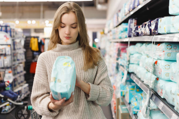 若い女性の母親は、ショップモールのスーパーマーケットでおむつを選びます。子供のための衛生用品。 - diaper shopping human pregnancy supermarket ストックフォトと画像