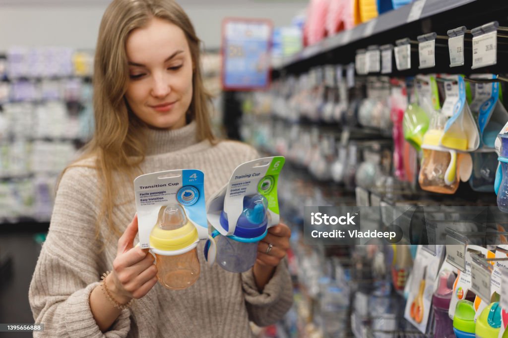 Young mother chooses sippy cup in shop Young mother chooses sippy cup in shop. Cup Stock Photo