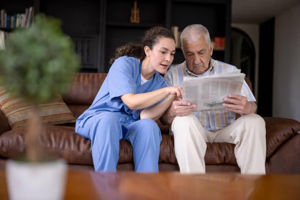 starszy mężczyzna czytający gazetę w domu z pomocą swojego opiekuna - nursing home senior adult home caregiver physical therapy zdjęcia i obrazy z banku zdjęć