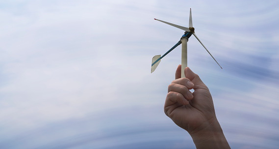 Hand holding a sustainable green energy wind turbine. The wind is moving through the turbines.