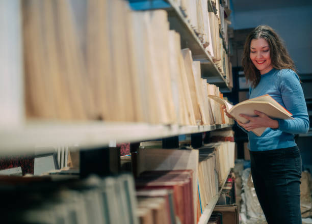 istock Beautiful university student standing by the shelf in the library and reading a book 1395663328