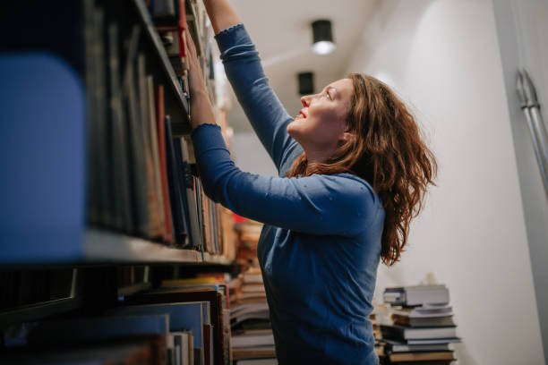 Beautiful university student reaching books on upper shelves in the library