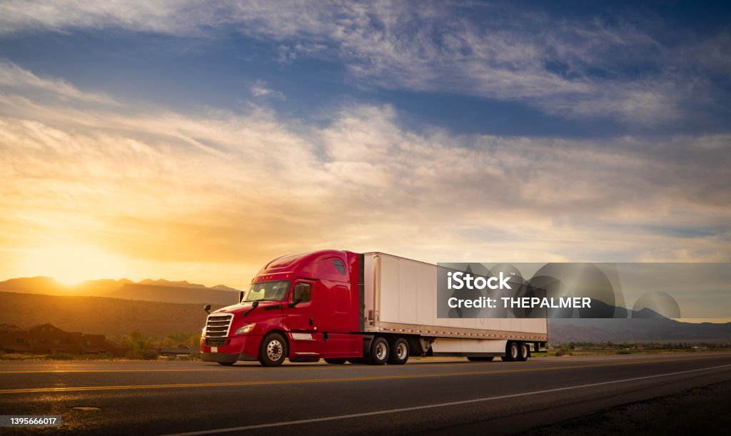 Red and white semi-truck speeding at sunrise on a single lane road USA Truck Stock Photo