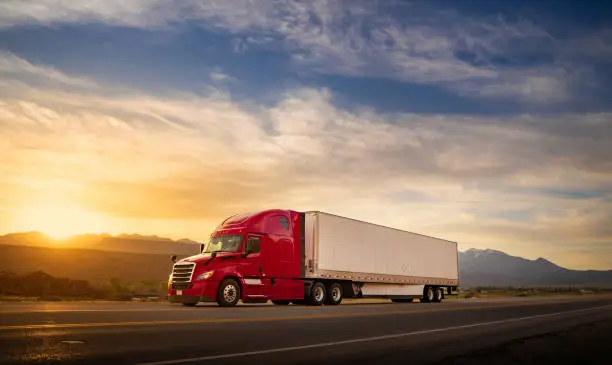 Photo of Red and white semi-truck speeding at sunrise on a single lane road USA