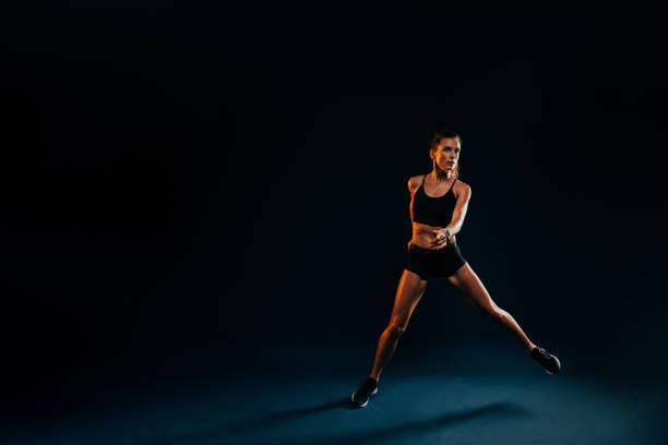 istock Healthy strong woman jumping from side to side on black background warming up 1395667233