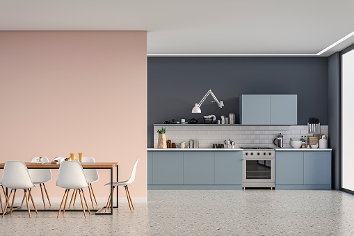 Empty modern kitchen with blue wooden kitchen cabinets on dark gray plaster wall,  white metro tiled background, full dining table and white chairs. A large powder pink plaster wall background on terrazzo floor with copy space and windows on a side. Retro style of 70's. 3D rendered image.