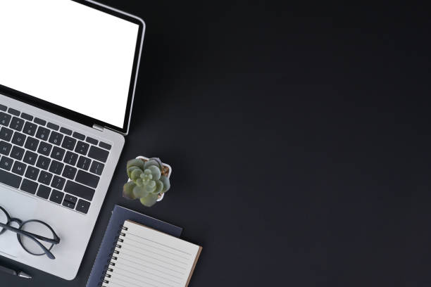 istock Black wooden table with notebook, laptop computer and eyeglasses. Flat lay, top view and copy space. 1395668448