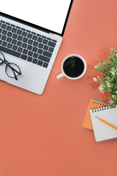 istock Mock up laptop with white display, coffee cup and notebook on orange background. Flay lay. 1395669292