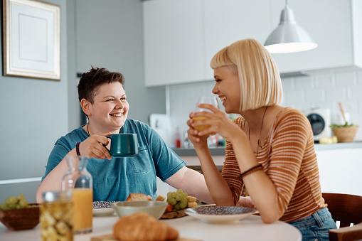 Happy lesbian and her girlfriend talking while having breakfast together at home.