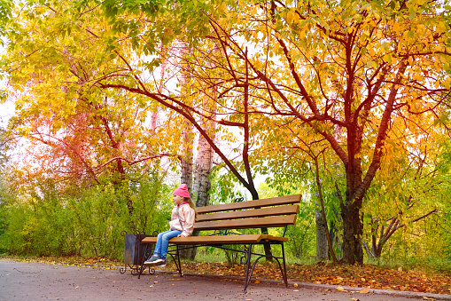 Little girl sitting on the bench alone. Autumn park. Beautiful in nature
