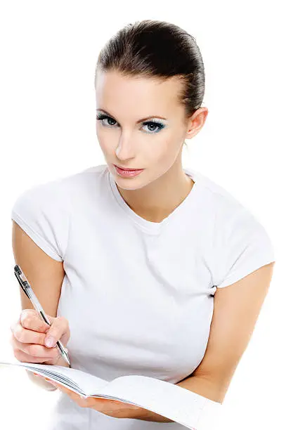 Portrait young beautiful dark-haired woman-student who writes in exercise book with pen, isolated on white background.