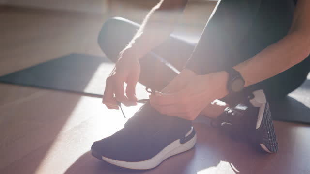 Woman maintaining healthy lifestyle, getting ready for work out, tying shoelaces and tightening the knot on her sports shoe