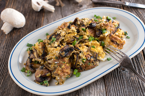 Delicious breakfast or lunch with scrambled eggs, mushrooms and  onions. Served on a plate on rustic and wooden table background. Ready to eat.