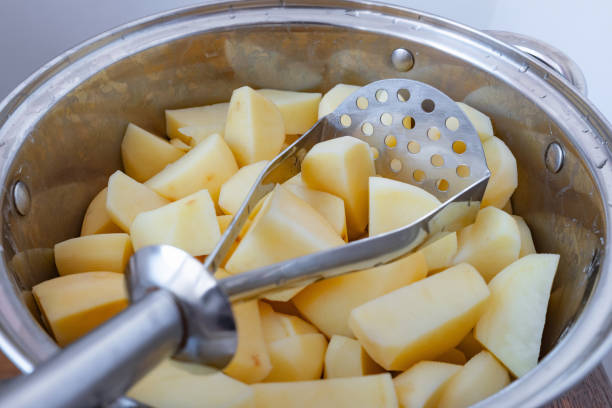 Potato masher in a pot with raw chopped potatoes stock photo