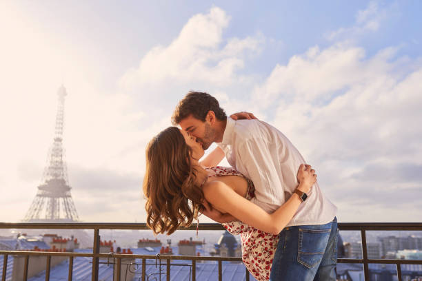 aufnahme eines jungen paares, das einen romantischen moment auf dem balkon einer wohnung mit blick auf den eiffelturm in paris, frankreich teilt - paris france eiffel tower love kissing stock-fotos und bilder