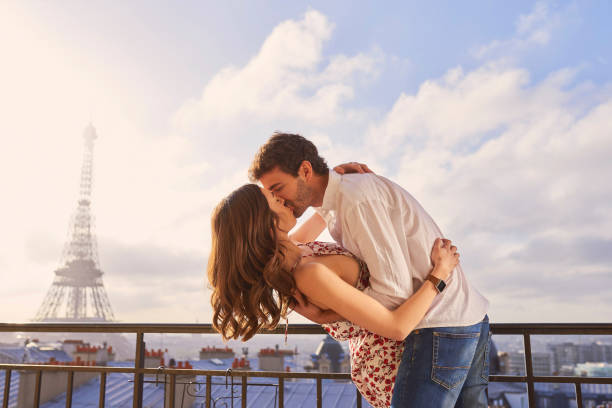 foto de una joven pareja compartiendo un momento romántico en el balcón de un apartamento con vistas a la torre eiffel en parís, francia - besar fotografías e imágenes de stock