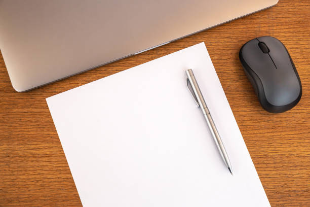 istock Minimal wooden work desktop with blank page with copy space, pen, laptop, keyboard, mouse. Top view, text space, mock up. Office desk. 1395681063