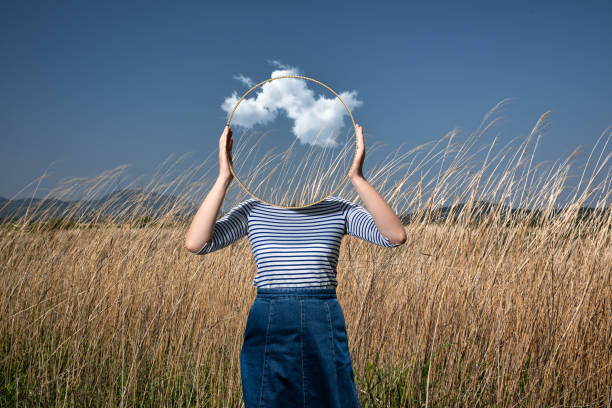 Surrealism_faceless_mirror Surrealism with a woman holding a mirror and covering her face in the field with a transparent background behind the mirror surreal stock pictures, royalty-free photos & images