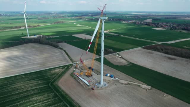 Wind turbine assembly, crane lifts the propeller. Windmill producing electricity under construction.