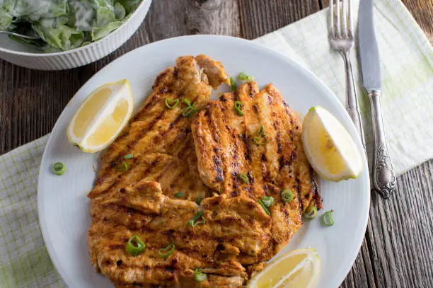 Fresh grilled and marinated chicken breast or steaks. Served ready to eat on a plate with lemon. Closeup and overhead view