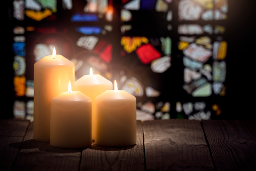 Candles burning in a church with stained glass window background