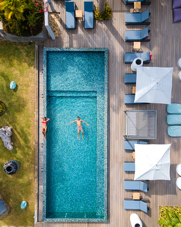 Drone aerial view from above at pool, Praslin Seychelles, couple men and women in the pool during vacation at a luxury resort at the beach of Anse Volbert tropical island with withe beaches and palm trees