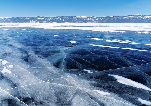Winter landscape with mountains and dark blue ice of Baikal Lake in Siberia with clear blue sky. Natural background.