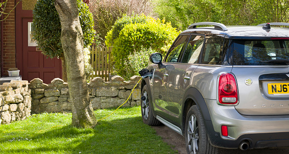 Buckinghamshire, UK - April 09, 2022. Electric car charging at home. Electric Mini Countryman parked outside a house, plugged in and recharging.
