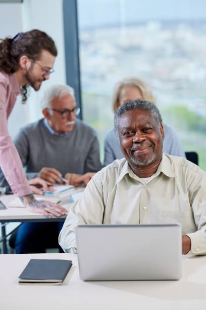 istock A senior african student smiling at the camera while group of multicultural senior students is discussing a programming project with an educator in the classroom. 1395693394