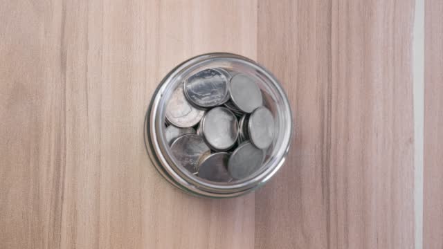 4K stop motion video, Rising coins in glass jars on wooden table, money saving and investment ideas. Top view view.