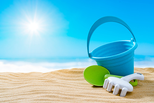 Summer backgrounds: blue sand bucket, shovel and pail on gold colored sand dune. The composition is at the right of an horizontal frame leaving useful copy space for text and/or logo at the left. High resolution 42Mp outdoors digital capture taken with SONY A7rII and Zeiss Batis 40mm F2.0 CF lens